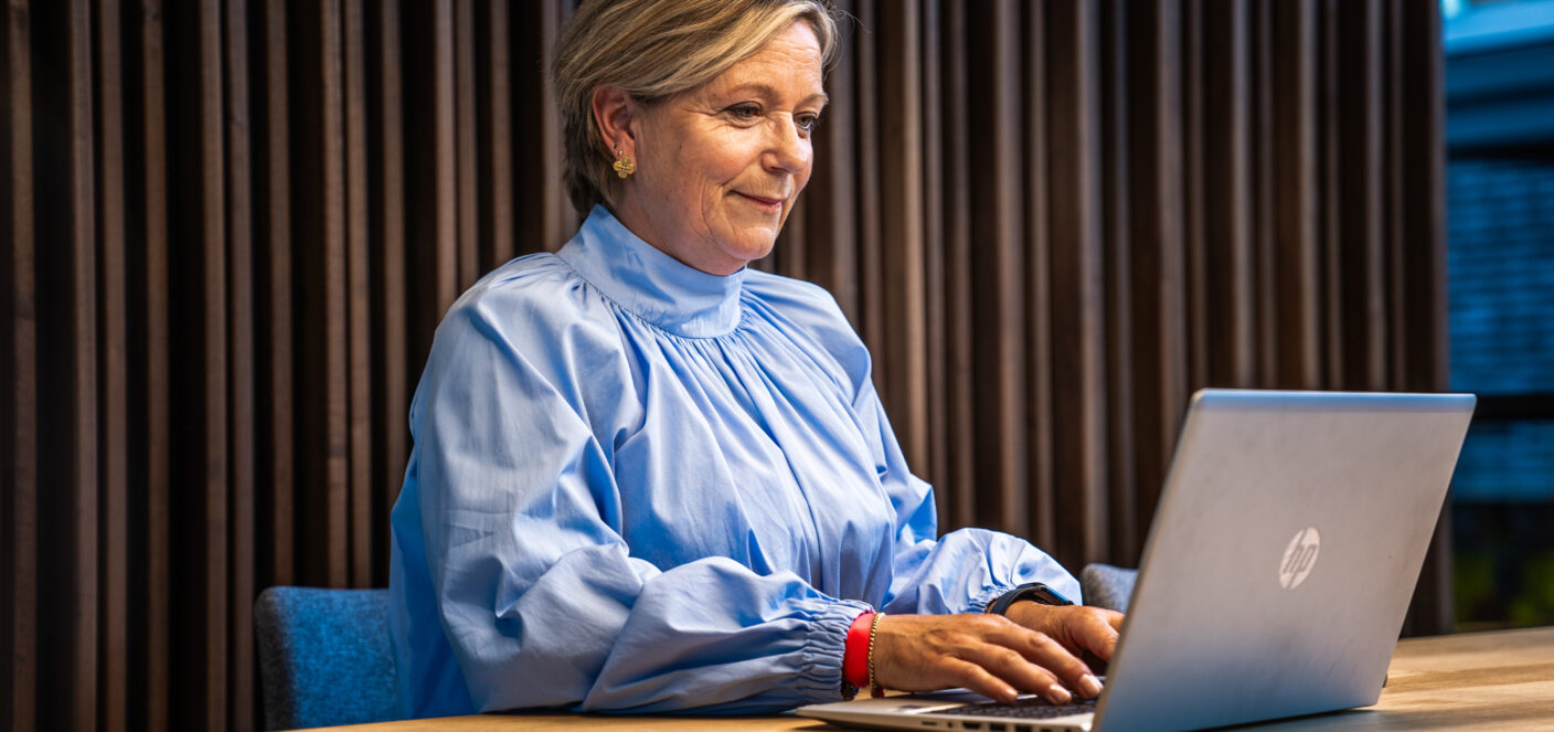 afbeelding van een vrouw die aan tafel zit achter een laptop.