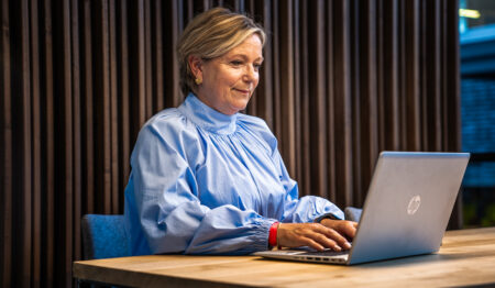 afbeelding van een vrouw die aan tafel zit achter een laptop.