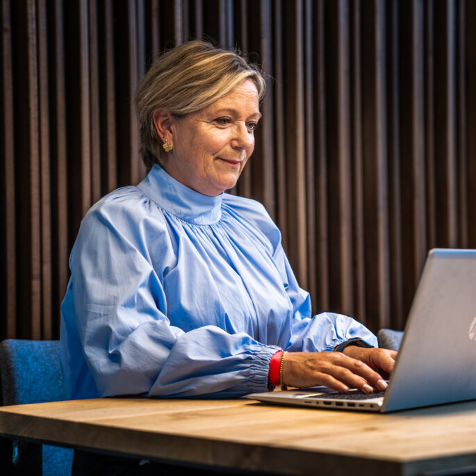 afbeelding van een vrouw die aan tafel zit achter een laptop.