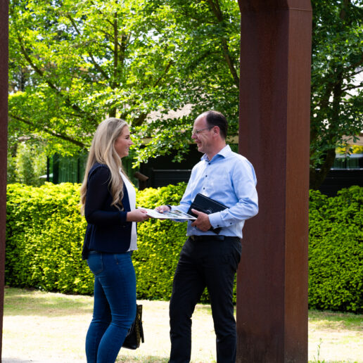 Man en vrouw staan buiten te praten. Man overhandigd mevrouw een brochure.