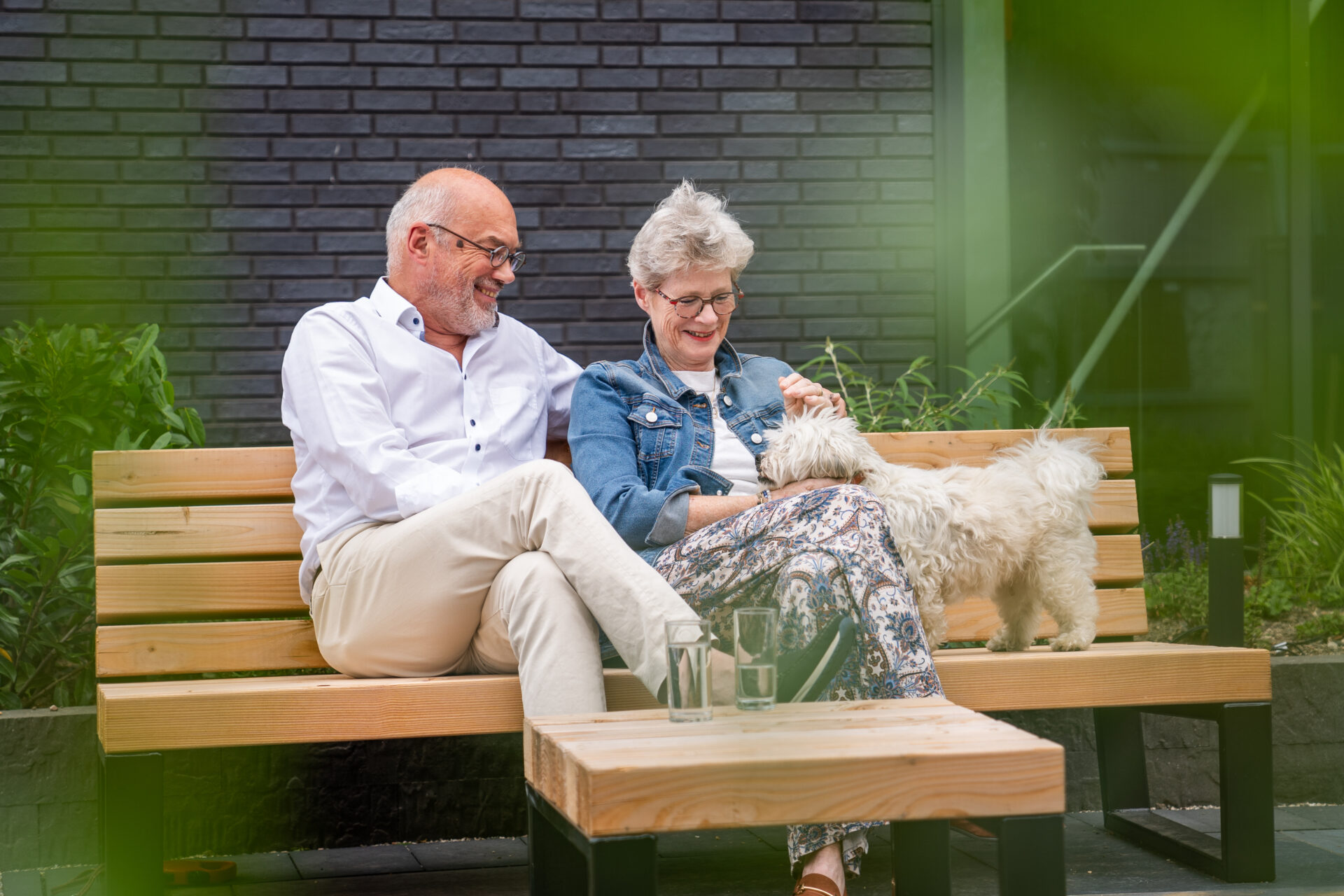 afbeelding van volwassen man en vrouw op houten bankje met hond.