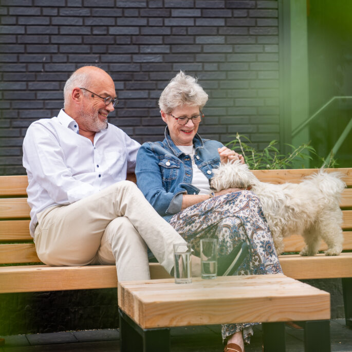 afbeelding van volwassen man en vrouw op houten bankje met hond.