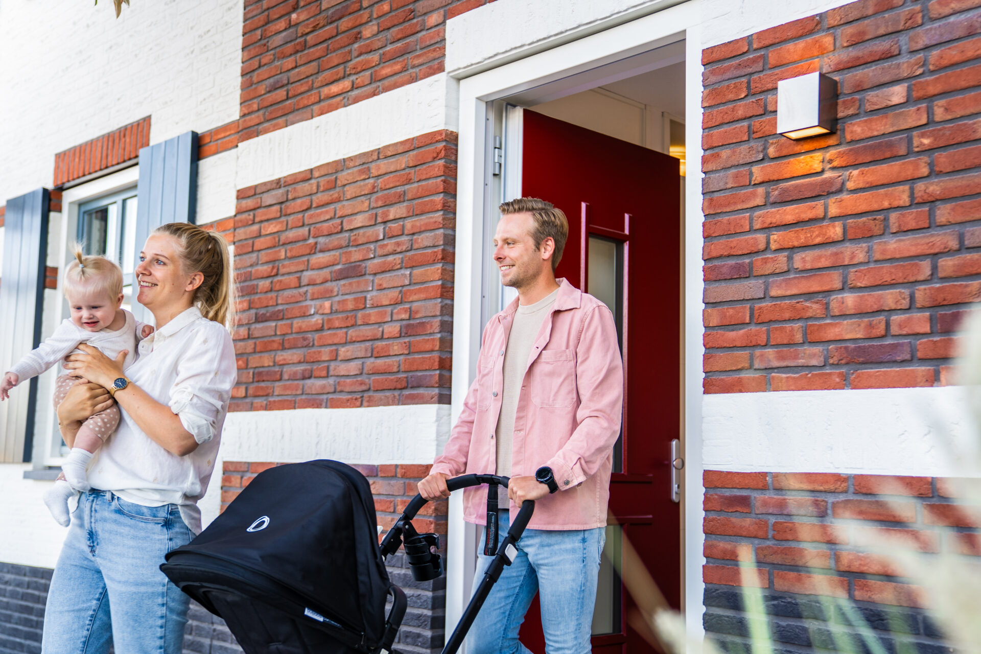 Afbeelding van jong gezin dat voordeur uitloopt. Moeder met kindje op de arm vader met de kinderwagen