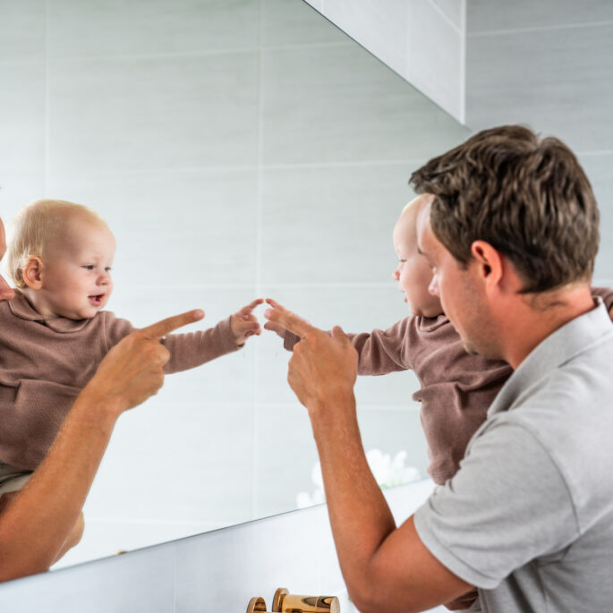 Jonge vader met baby voor de spiegel.