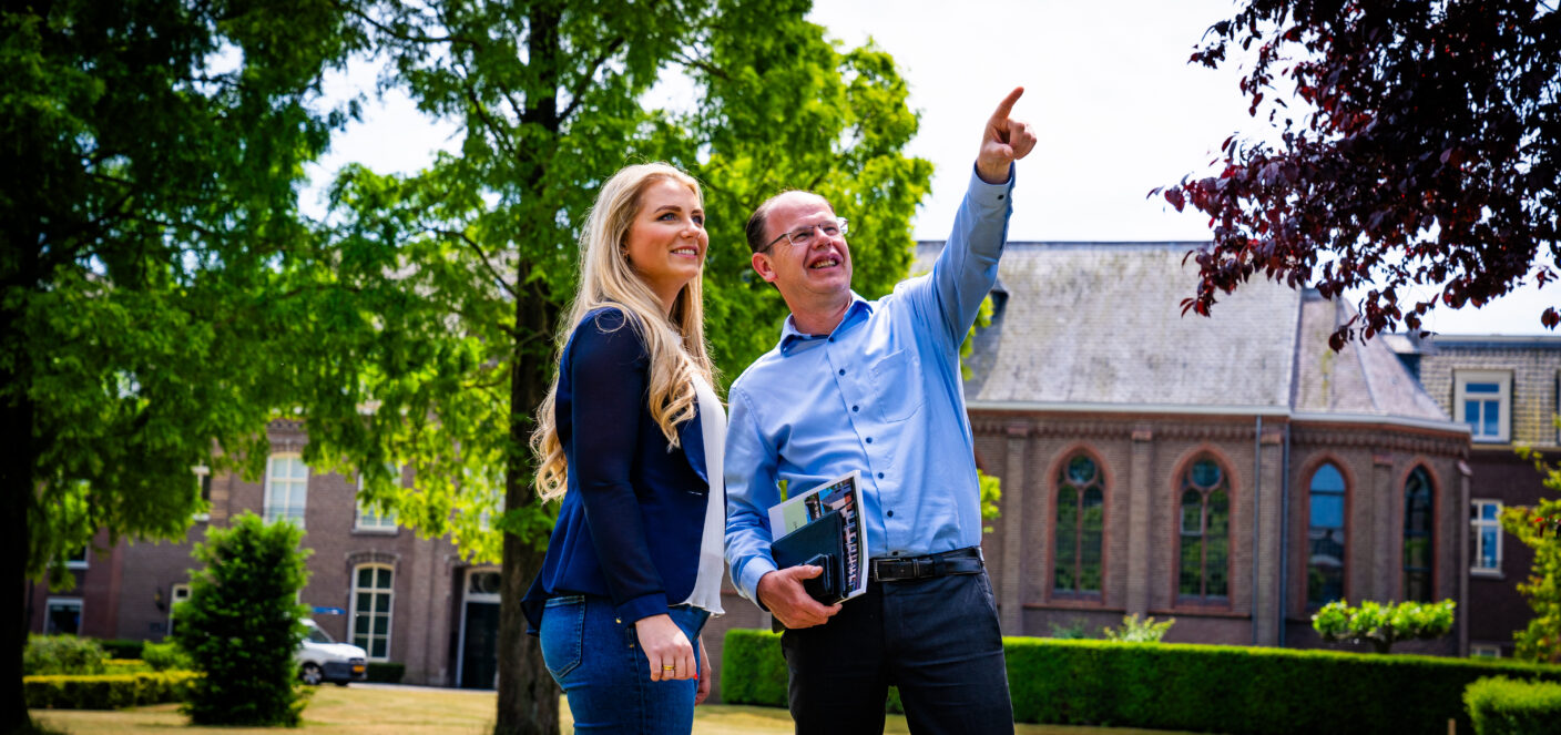 afbeelding van twee werknemers die buiten staan met een brochure in hun hand. de een wijst omhoog