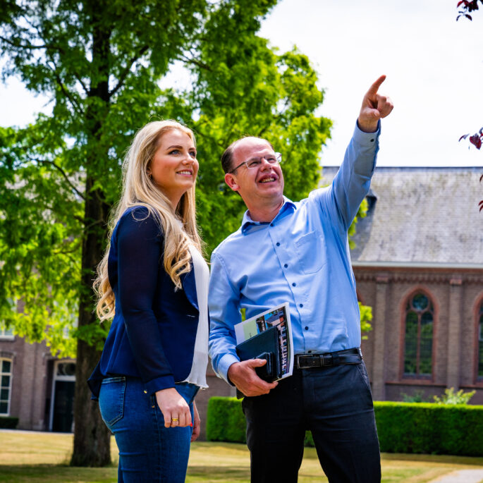 afbeelding van twee werknemers die buiten staan met een brochure in hun hand. de een wijst omhoog