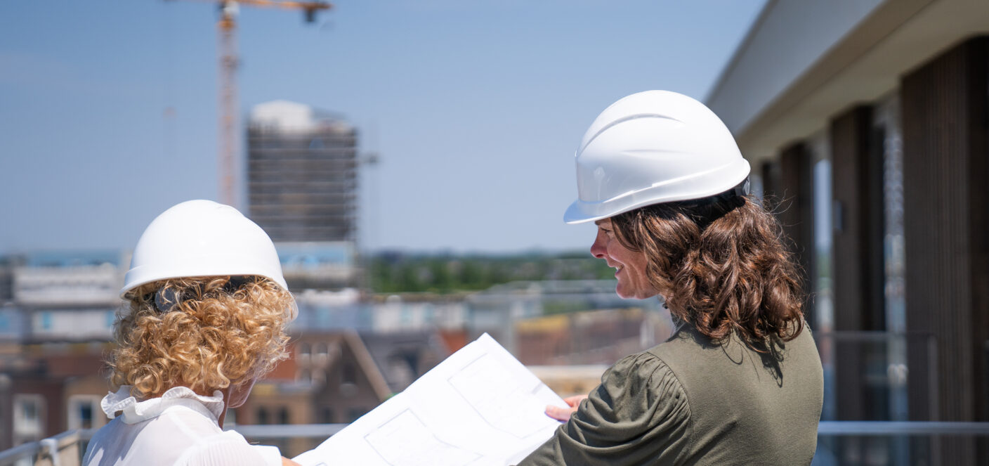 twee vrouwen met een bouwhelm op, op de bouw die kijken naar een technische tekening